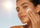 Mulher aplicando protetor solar no rosto para ilustrar a diferença entre proteção UVA, UVB e luz visível.