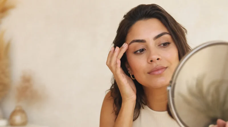 Mulher observando sobrancelhas recém-aplicadas em um espelho com expressão de dúvida