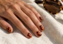 Unhas curtas com efeito tartaruga em âmbar e marrom, ao lado de óculos com estampa semelhante.