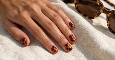 Unhas curtas com efeito tartaruga em âmbar e marrom, ao lado de óculos com estampa semelhante.