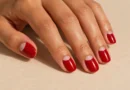 Unhas meia-lua com esmalte vermelho e semicírculo transparente próximo às cutículas.